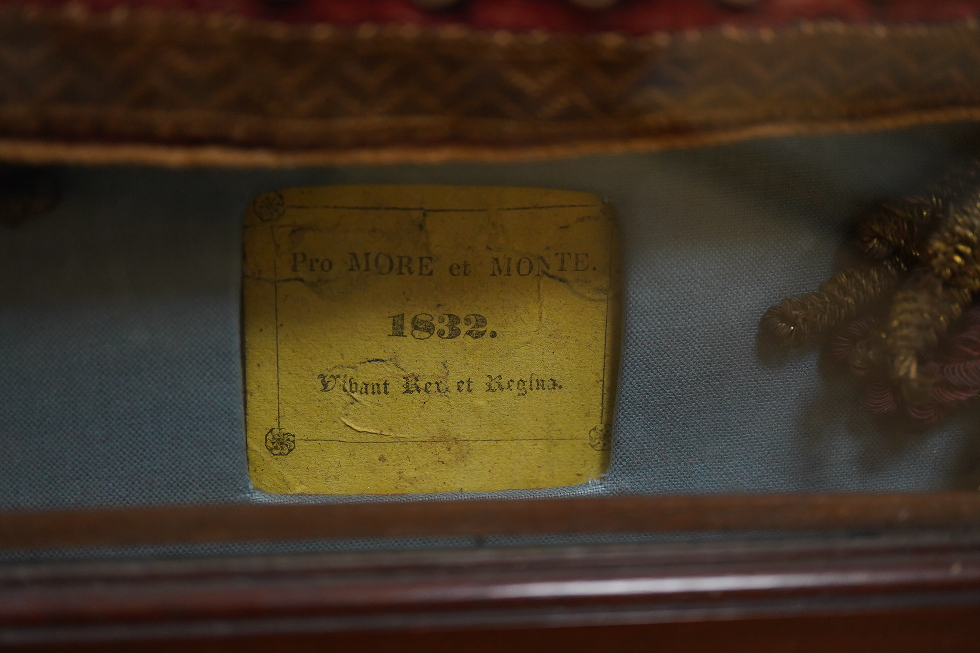 Eton interest - a commemorative William IV, ceremonial red velvet, gold metallic thread, tasselled and braided bag, mounted within a mahogany glazed cabinet. An old printed ticket in Latin mounted beneath: Pro More et Mo